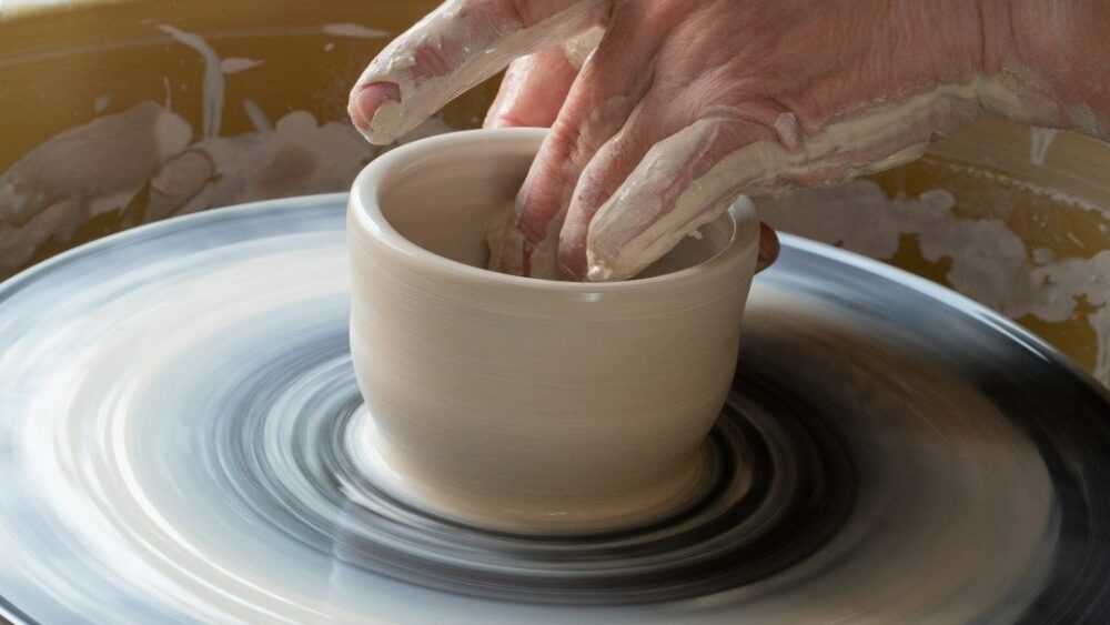Potter's hands shape a clay vessel on a spinning wheel